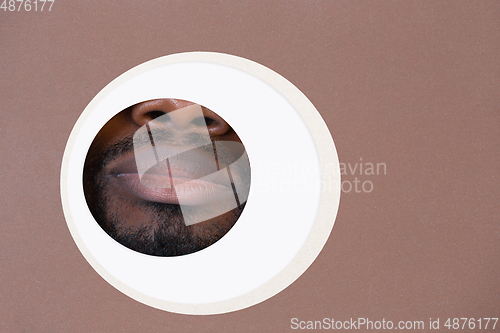 Image of Lips of african-american man peeking throught circle in brown background