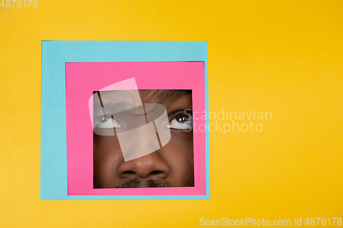 Image of Face of african-american man peeking throught square in yellow background