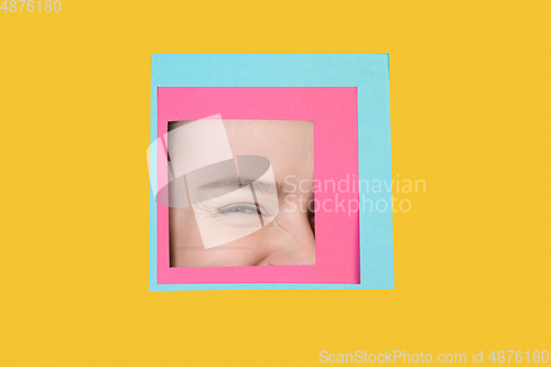 Image of Face of caucasian woman peeking throught square in yellow background