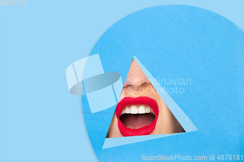 Image of Female red lips peeking throught triangle in blue background