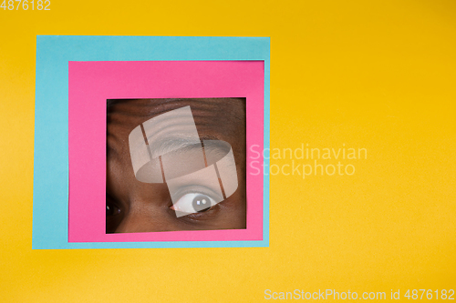 Image of Eye of african-american man peeking throught square in yellow background