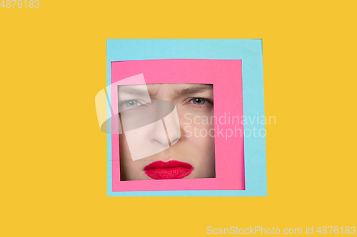Image of Face of caucasian woman peeking throught square in yellow background