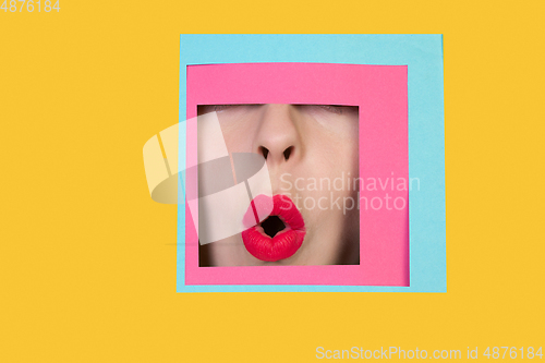 Image of Face of caucasian woman peeking throught square in yellow background