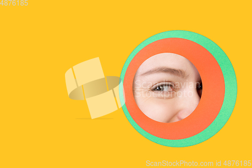 Image of Female eye peeking throught circle in yellow background
