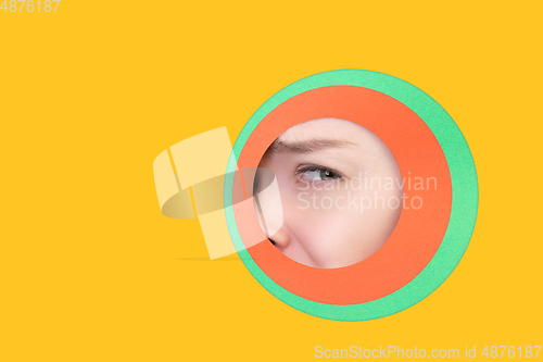 Image of Female eye peeking throught circle in yellow background