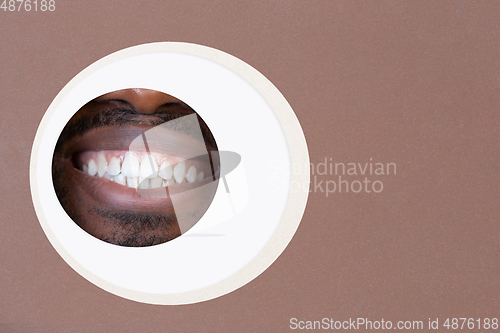 Image of Lips of african-american man peeking throught circle in brown background