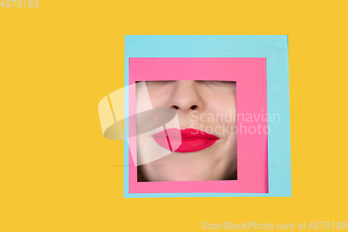 Image of Face of caucasian woman peeking throught square in yellow background