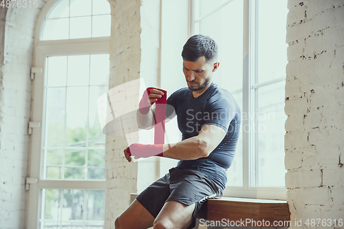 Image of Young caucasian man training at home during quarantine of coronavirus outbreak, doing exercises of fitness, aerobic. Staying sportive during insulation.