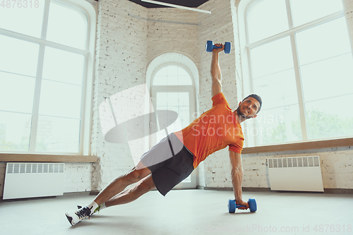 Image of Young caucasian man training at home during quarantine of coronavirus outbreak, doing exercises of fitness, aerobic. Staying sportive during insulation.