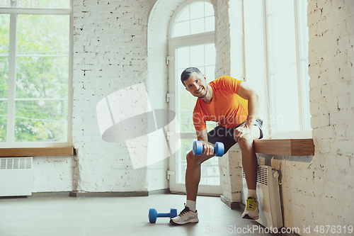 Image of Young caucasian man training at home during quarantine of coronavirus outbreak, doing exercises of fitness, aerobic. Staying sportive during insulation.