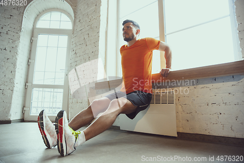 Image of Young caucasian man training at home during quarantine of coronavirus outbreak, doing exercises of fitness, aerobic. Staying sportive during insulation.