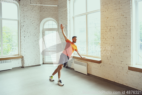 Image of Young caucasian man training at home during quarantine of coronavirus outbreak, doing exercises of fitness, aerobic. Staying sportive during insulation.