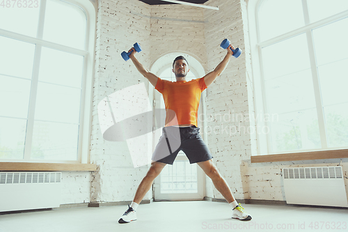 Image of Young caucasian man training at home during quarantine of coronavirus outbreak, doing exercises of fitness, aerobic. Staying sportive during insulation.