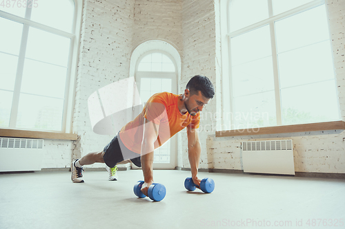 Image of Young caucasian man training at home during quarantine of coronavirus outbreak, doing exercises of fitness, aerobic. Staying sportive during insulation.