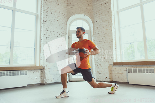 Image of Young caucasian man training at home during quarantine of coronavirus outbreak, doing exercises of fitness, aerobic. Staying sportive during insulation.