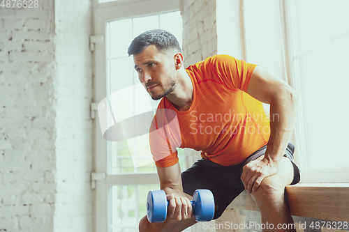 Image of Young caucasian man training at home during quarantine of coronavirus outbreak, doing exercises of fitness, aerobic. Staying sportive during insulation.