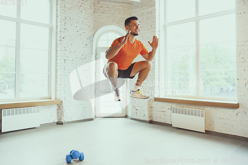 Image of Young caucasian man training at home during quarantine of coronavirus outbreak, doing exercises of fitness, aerobic. Staying sportive during insulation.