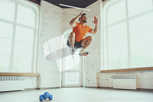 Image of Young caucasian man training at home during quarantine of coronavirus outbreak, doing exercises of fitness, aerobic. Staying sportive during insulation.