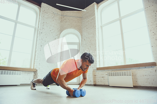 Image of Young caucasian man training at home during quarantine of coronavirus outbreak, doing exercises of fitness, aerobic. Staying sportive during insulation.