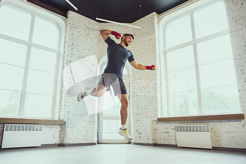 Image of Young caucasian man training at home during quarantine of coronavirus outbreak, doing exercises of fitness, aerobic. Staying sportive during insulation.