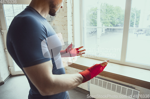 Image of Young caucasian man training at home during quarantine of coronavirus outbreak, doing exercises of fitness, aerobic. Staying sportive during insulation.