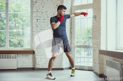 Image of Young caucasian man training at home during quarantine of coronavirus outbreak, doing exercises of fitness, aerobic. Staying sportive during insulation.