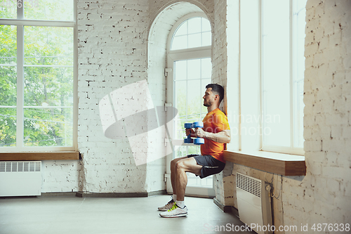 Image of Young caucasian man training at home during quarantine of coronavirus outbreak, doing exercises of fitness, aerobic. Staying sportive during insulation.