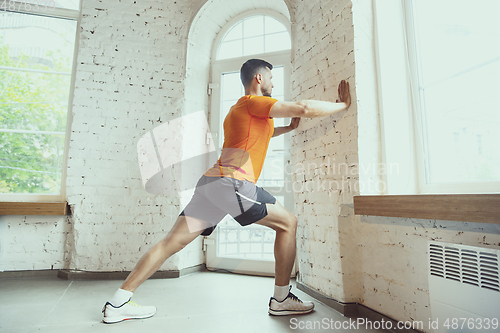 Image of Young caucasian man training at home during quarantine of coronavirus outbreak, doing exercises of fitness, aerobic. Staying sportive during insulation.