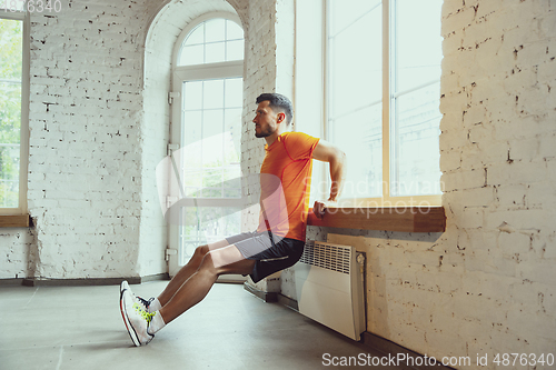 Image of Young caucasian man training at home during quarantine of coronavirus outbreak, doing exercises of fitness, aerobic. Staying sportive during insulation.