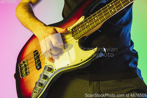 Image of Close up musician hands playing bass guitar on gradient studio background in neon light