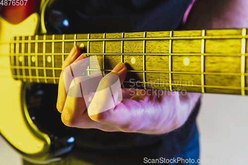 Image of Close up musician hands playing bass guitar on gradient studio background in neon light