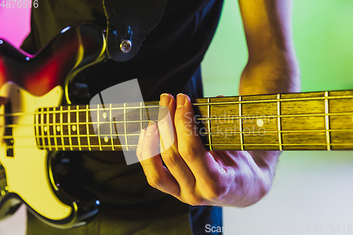 Image of Close up musician hands playing bass guitar on gradient studio background in neon light