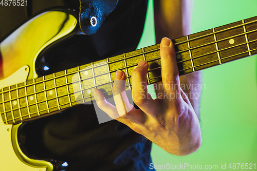 Image of Close up musician hands playing bass guitar on gradient studio background in neon light