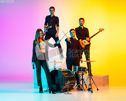 Image of Young caucasian musicians, band performing in neon light on gradient studio background