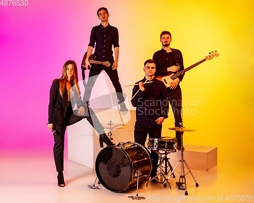 Image of Young caucasian musicians, band performing in neon light on gradient studio background