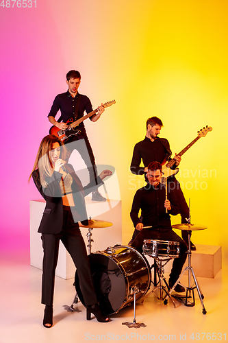 Image of Young caucasian musicians, band performing in neon light on gradient studio background