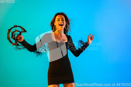 Image of Caucasian female singer with tambourin isolated on blue studio background in neon light