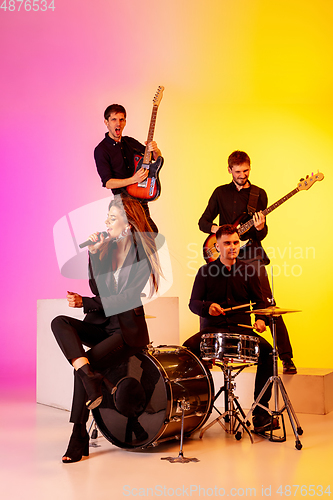 Image of Young caucasian musicians, band performing in neon light on gradient studio background