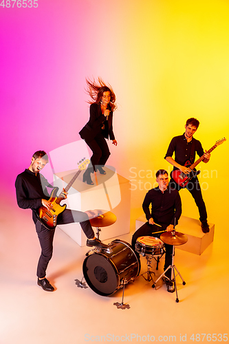 Image of Young caucasian musicians, band performing in neon light on gradient studio background