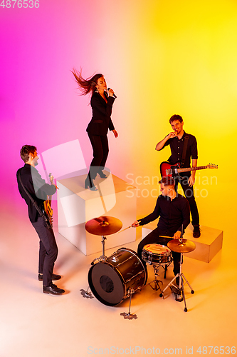 Image of Young caucasian musicians, band performing in neon light on gradient studio background