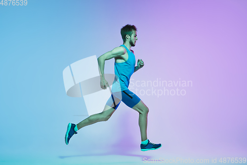 Image of Full length portrait of active young caucasian running, jogging man on gradient studio background in neon light