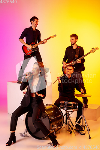 Image of Young caucasian musicians, band performing in neon light on gradient studio background