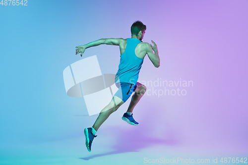 Image of Full length portrait of active young caucasian running, jogging man on gradient studio background in neon light