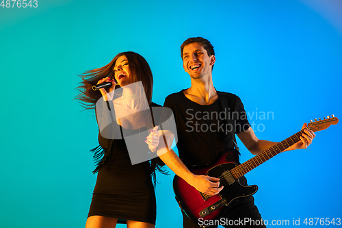 Image of Caucasian musicians, singer and guitarist, isolated on blue studio background in neon light