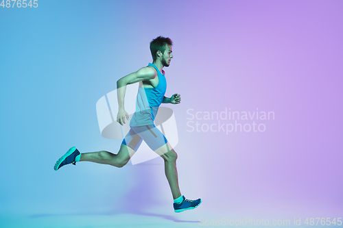 Image of Full length portrait of active young caucasian running, jogging man on gradient studio background in neon light