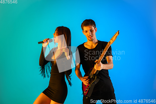 Image of Caucasian musicians, singer and guitarist, isolated on blue studio background in neon light