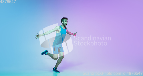 Image of Full length portrait of active young caucasian running, jogging man on gradient studio background in neon light