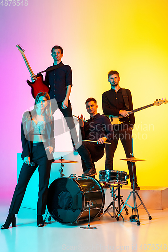 Image of Young caucasian musicians, band performing in neon light on gradient studio background