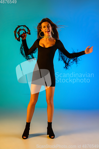 Image of Caucasian female singer with tambourin isolated on blue studio background in neon light