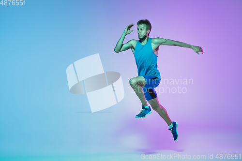 Image of Full length portrait of active young caucasian running, jogging man on gradient studio background in neon light